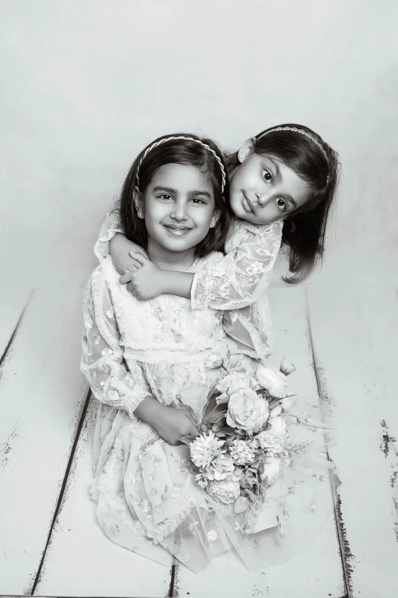 Black and white photograph of two sisters standing together with a soft toy