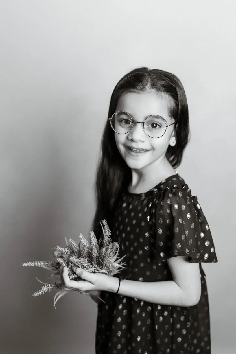 Black and white portrait of a girl wearing glasses and holding flowers