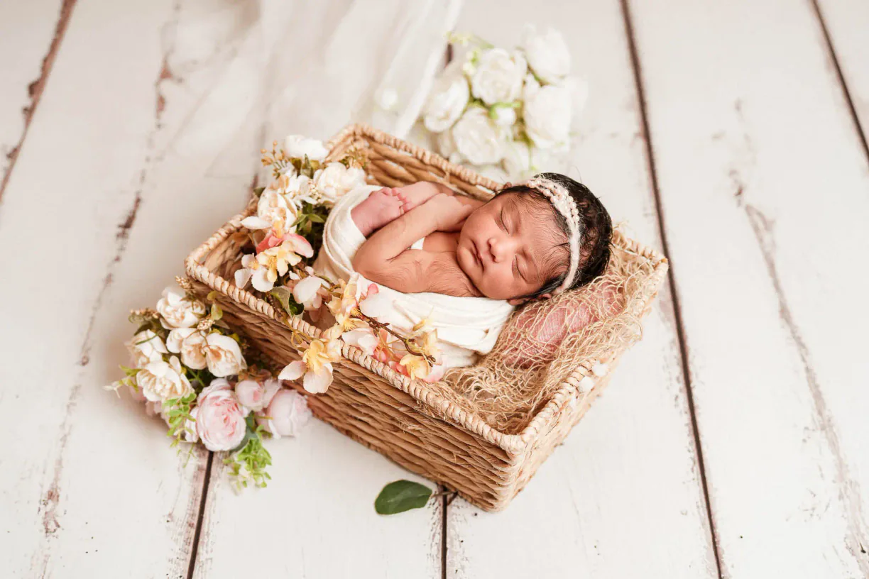 Sleeping newborn baby in a flower-lined basket during an at-home photoshoot