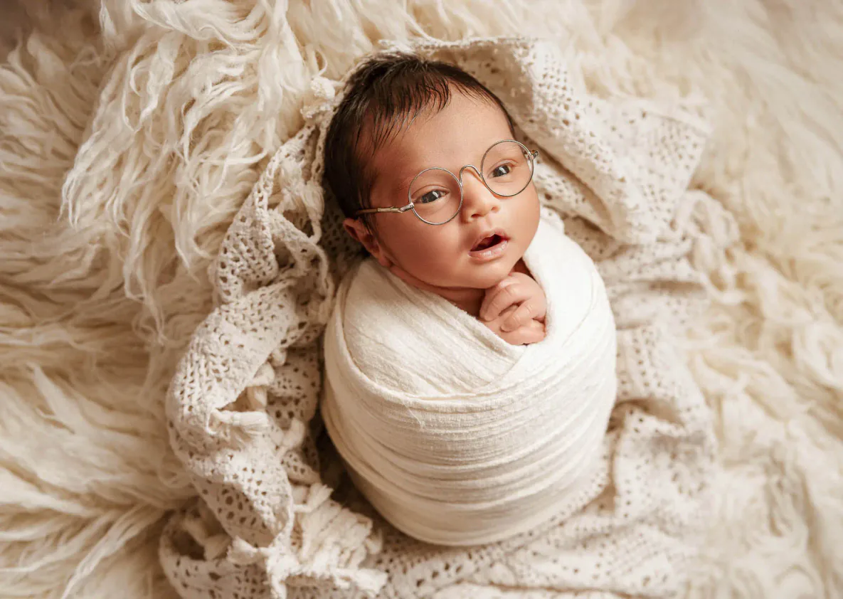 Awake newborn baby wrapped in cream fabric on a soft blanket