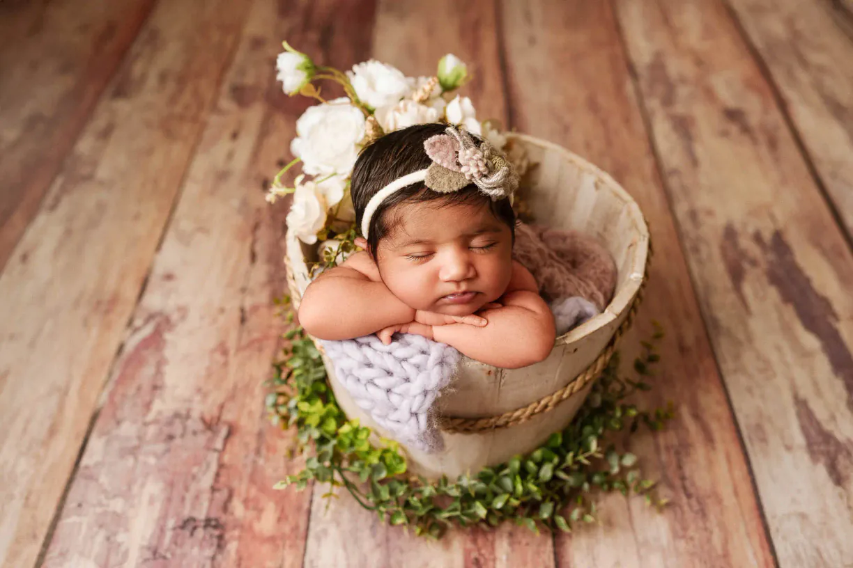 Sleeping newborn baby with a floral headband in a small basket