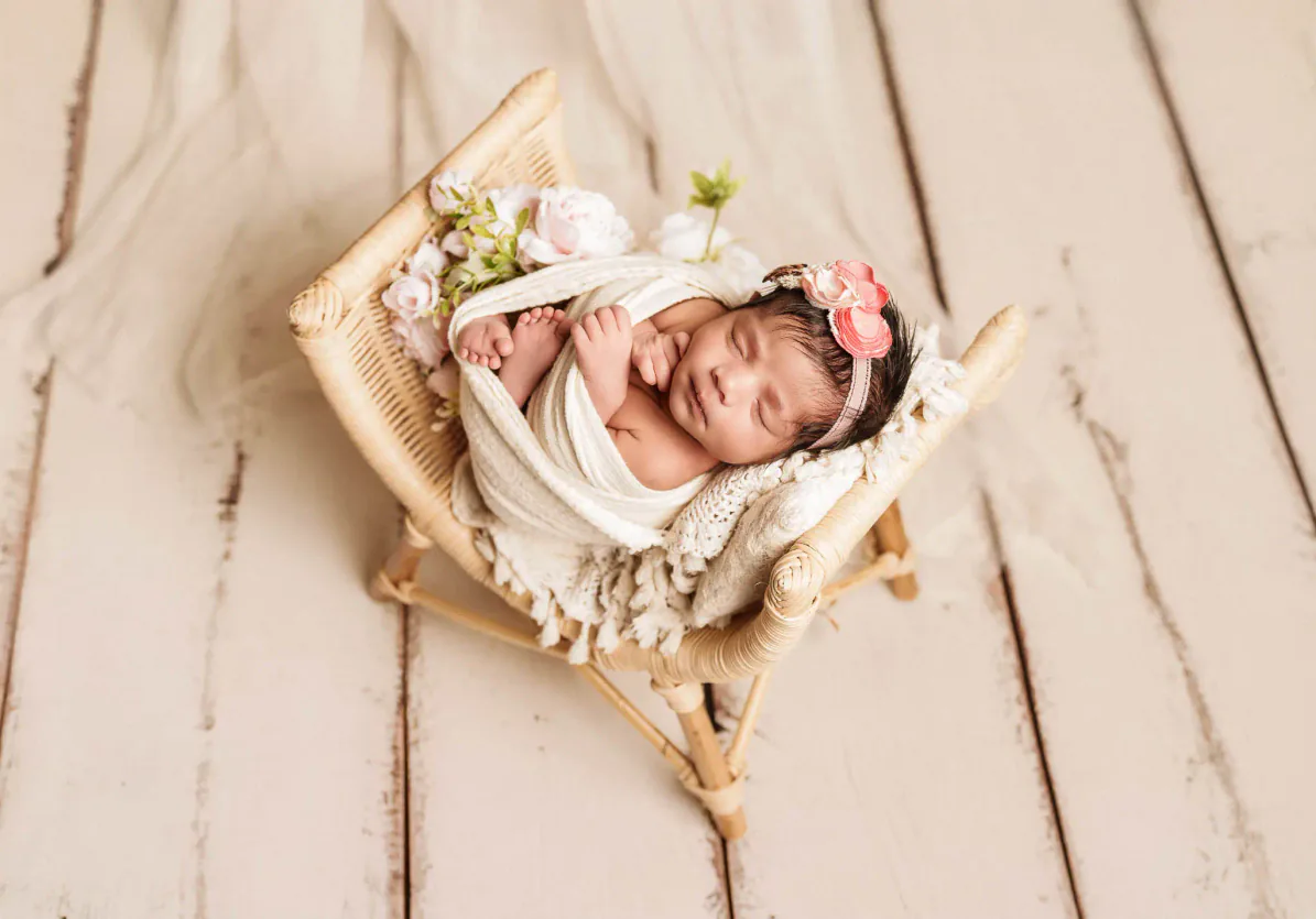 Wrapped newborn baby in a rustic basket with pale flowers