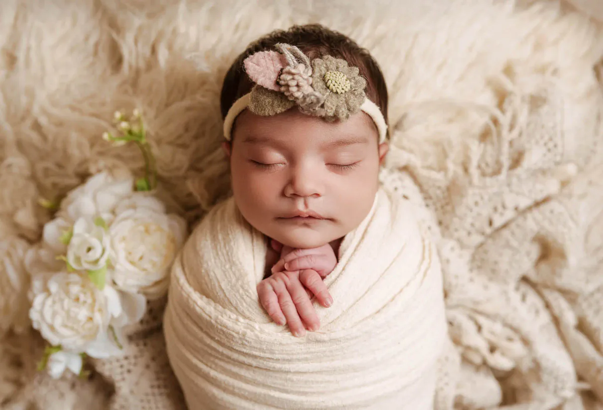 Close newborn portrait with baby wrapped in cream fabric and a flower headband