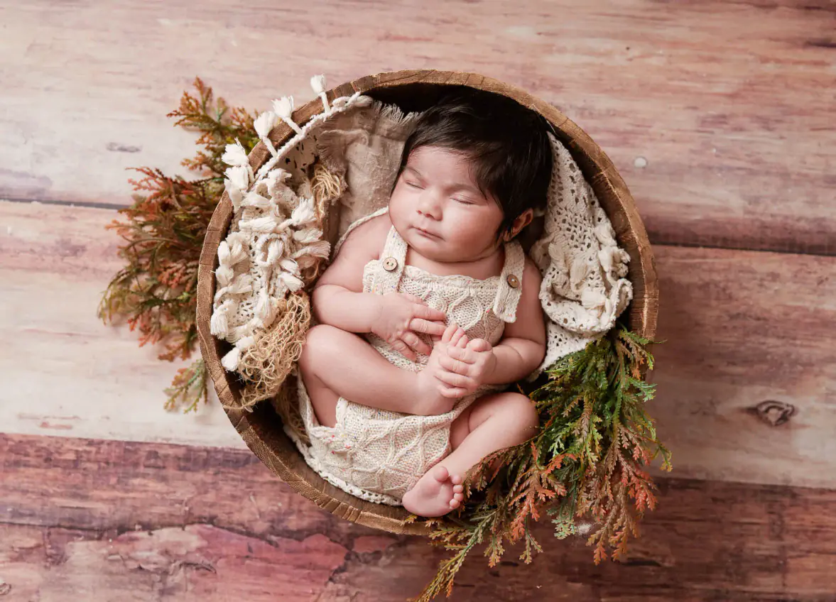 Sleeping newborn baby in a flower-lined basket on a wooden backdrop