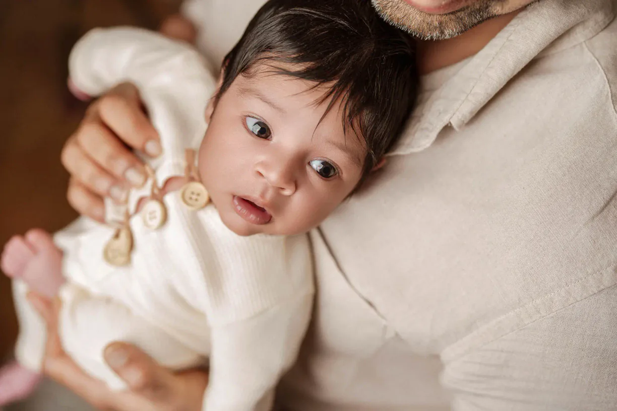 Baby looking towards the camera while resting in a parent's arms