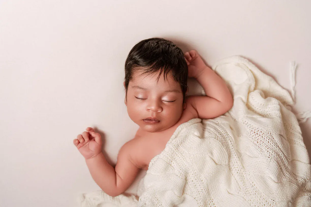 Newborn baby resting on a white blanket with one arm raised