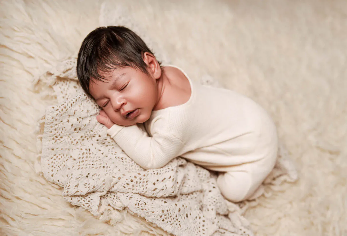 Sleeping baby curled on a textured cream blanket