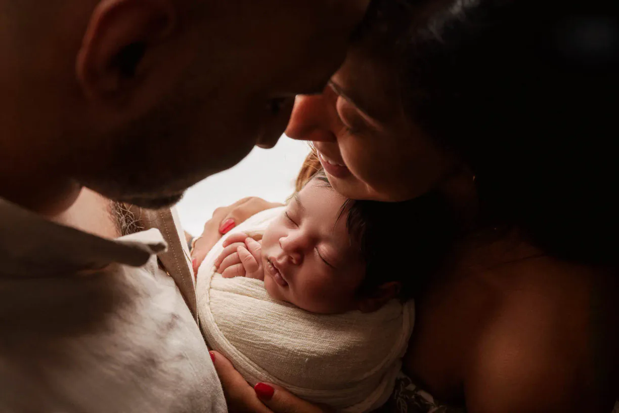 Parents close to their newborn baby in a warmly lit family photograph