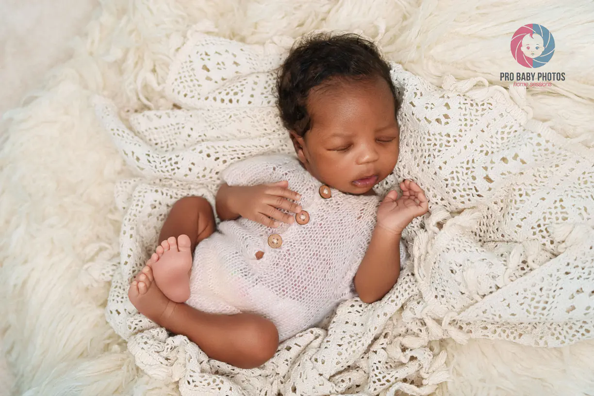 Newborn baby lying on a soft white blanket with a pale pink wrap