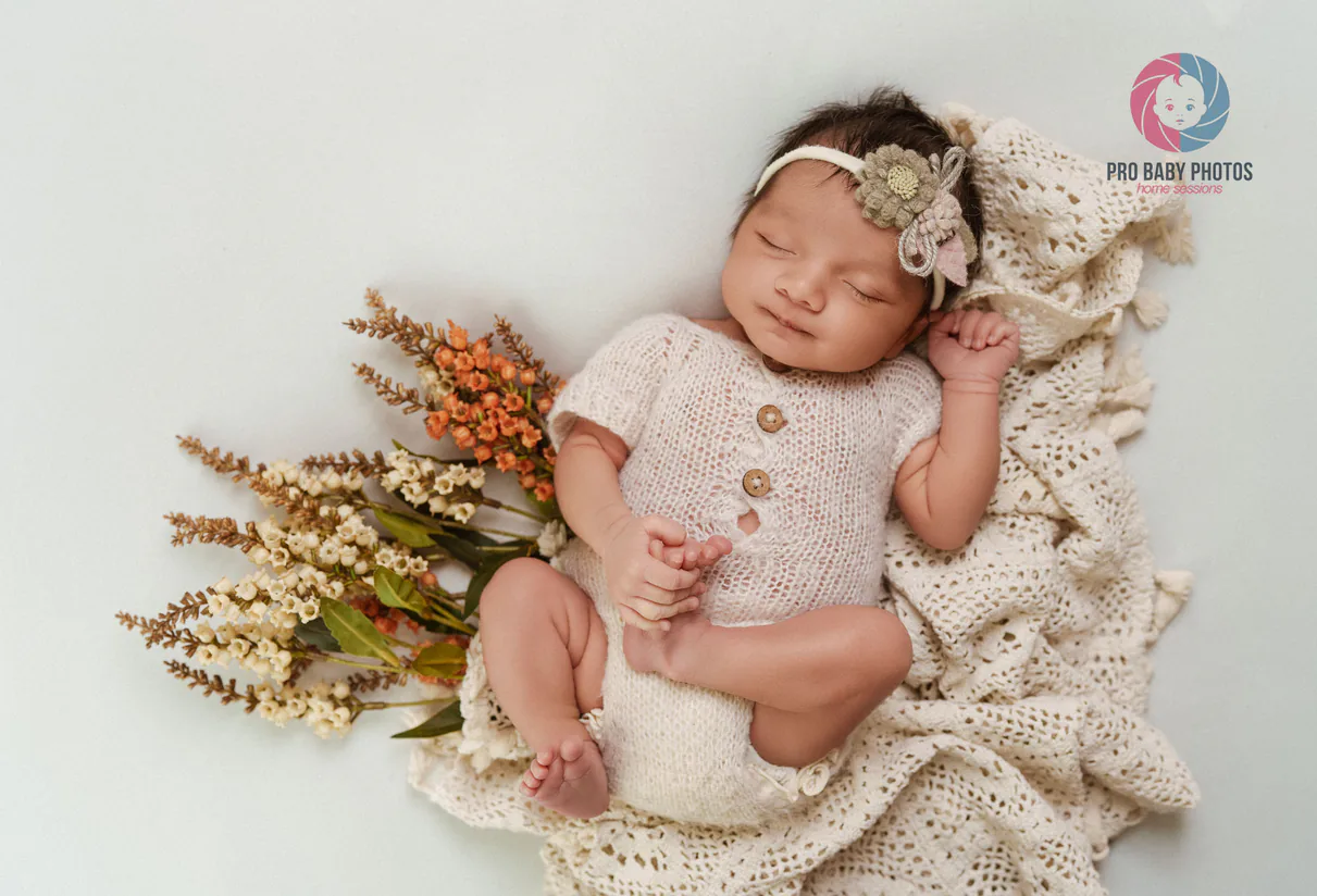 Newborn baby lying in a pale wrap with dried flowers nearby