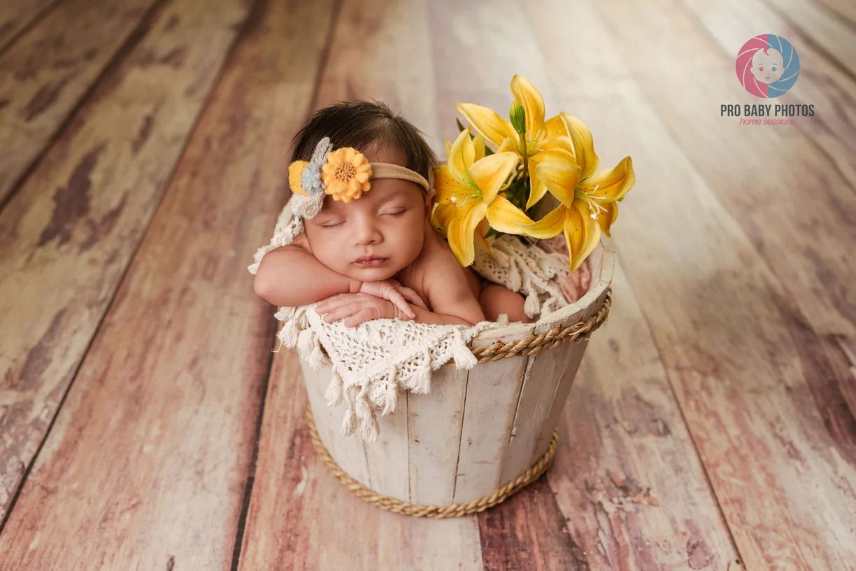 Sleeping baby in a small wooden bucket beside yellow flowers