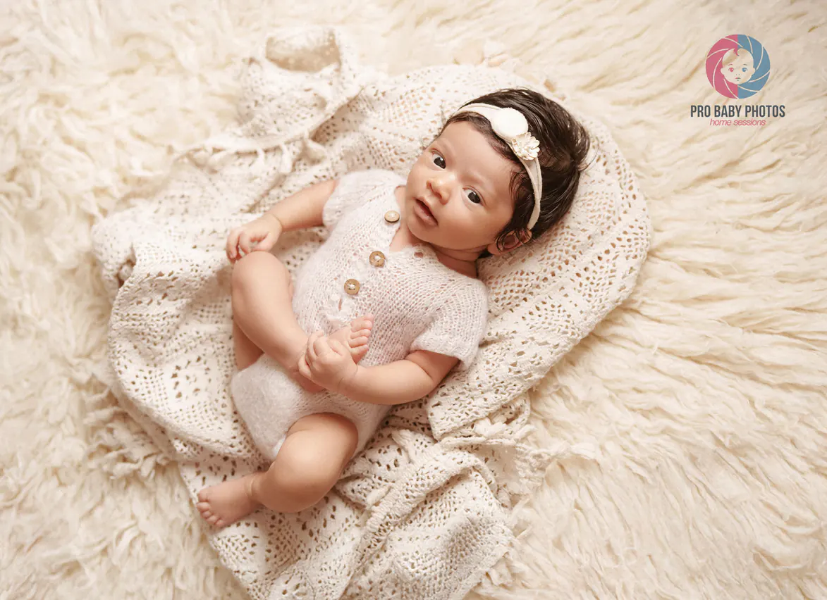 Newborn baby in a cream outfit resting on a textured blanket
