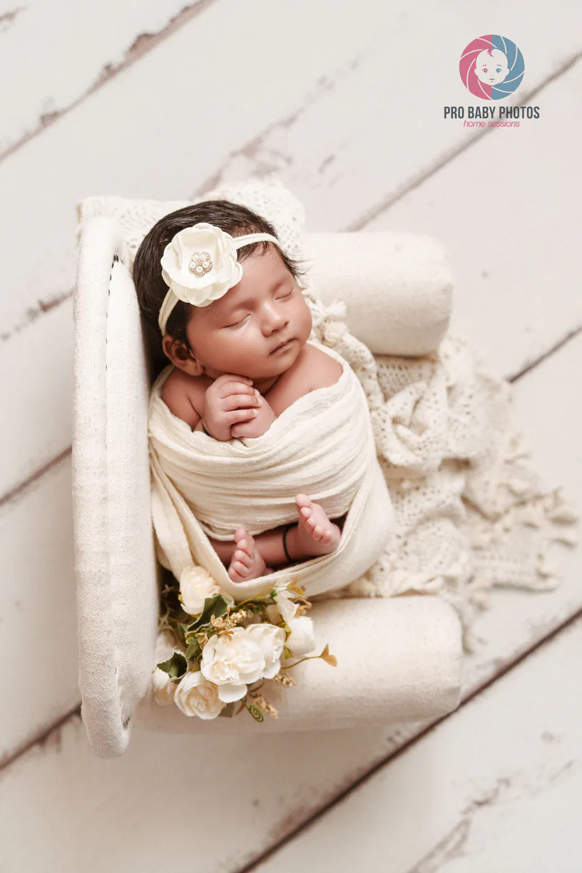 Wrapped newborn baby in a small wooden swing with flowers nearby