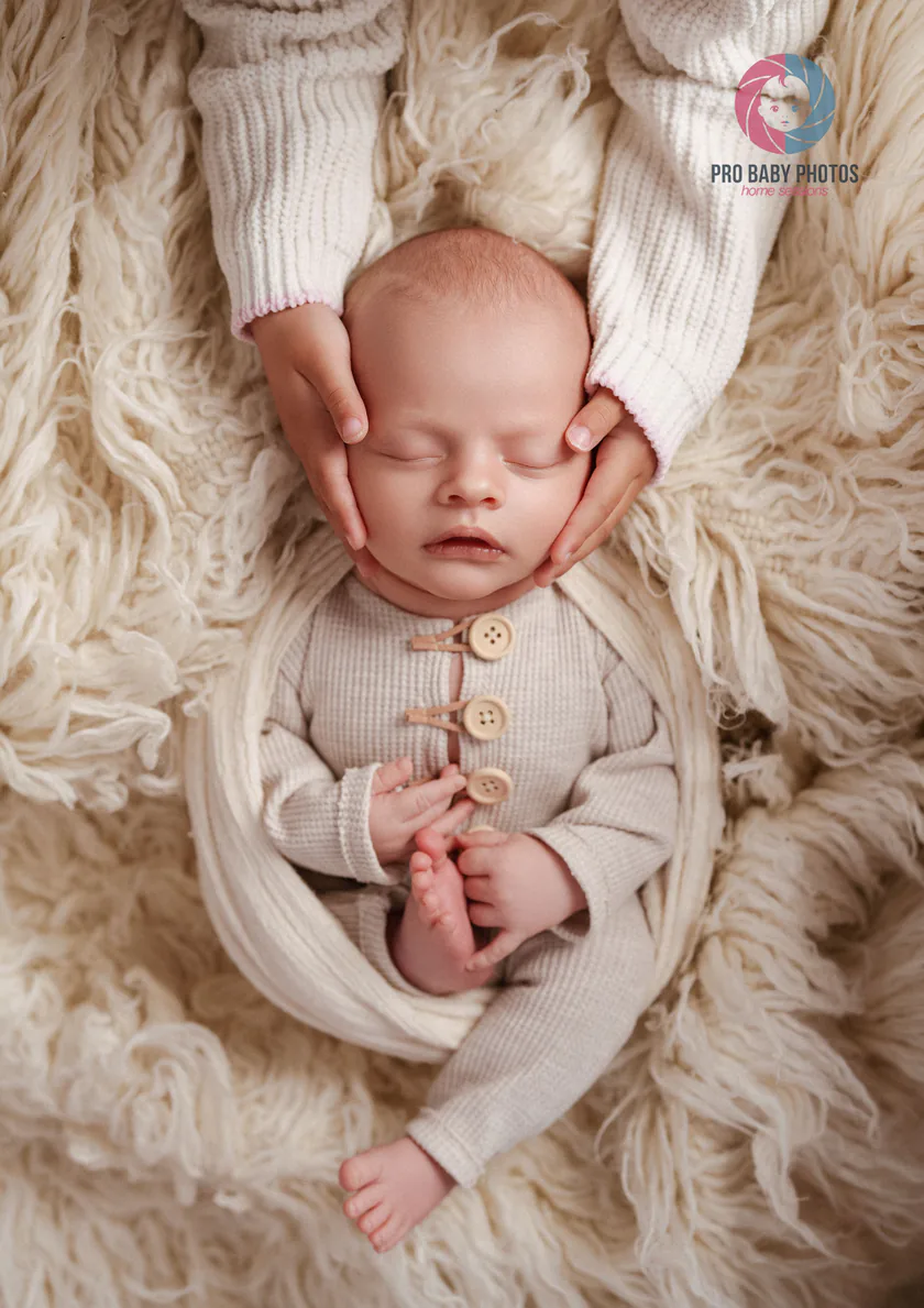 Newborn baby resting on a cream blanket with family hands nearby
