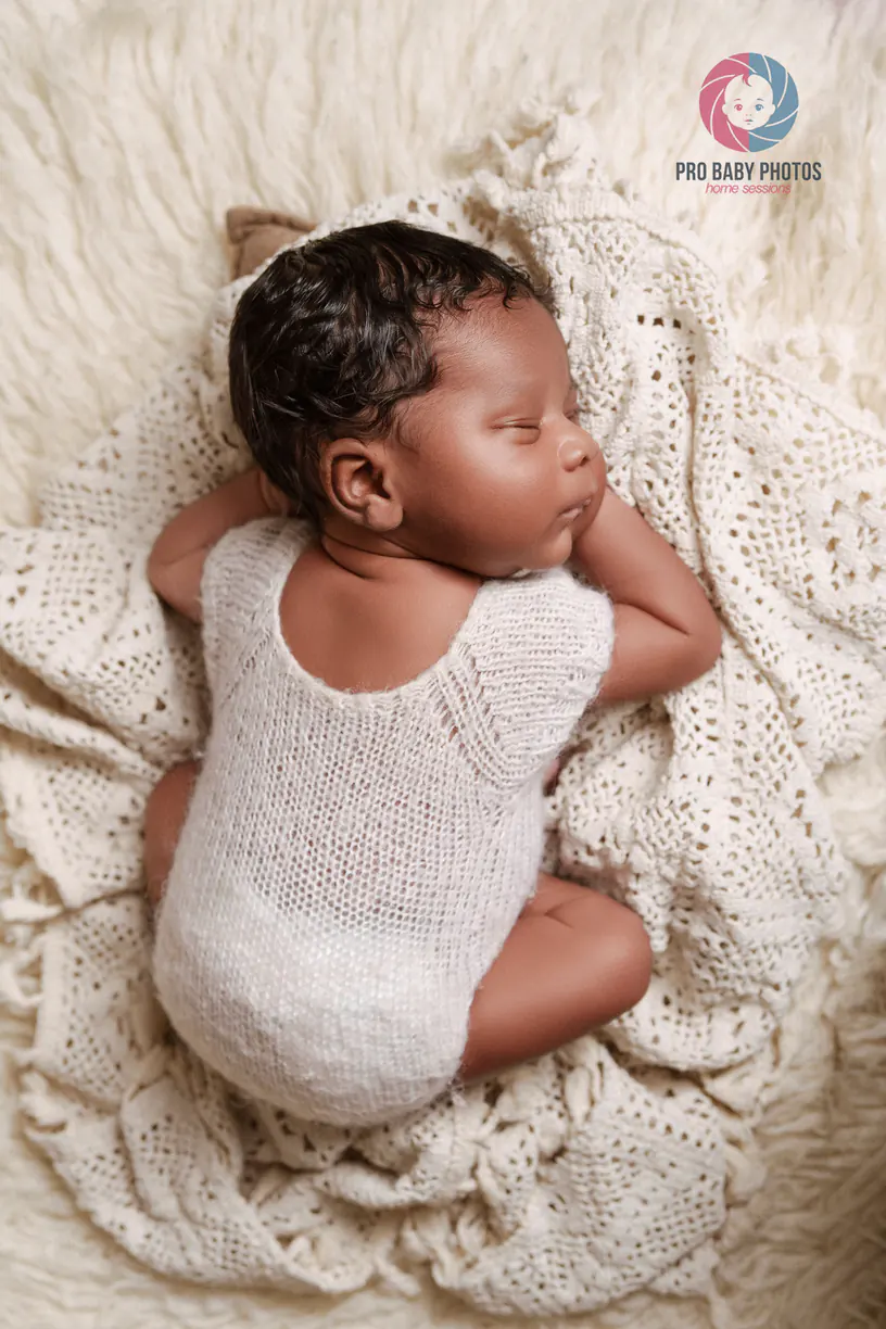 Baby in a pale outfit looking sideways on a soft blanket